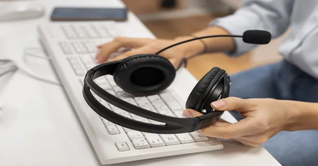 Close-up of hands holding an ergonomic Bluetooth headset with padded earcups and a boom microphone, highlighting its design for clear phone calls and comfortable office communication.