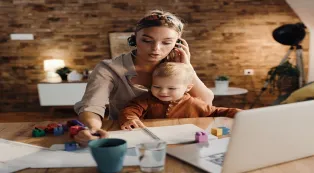 Working mother wearing a headset while taking a conference call at home with her child