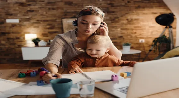 Working mother wearing a headset while taking a conference call at home with her child