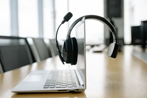 Professional communication headset mounted on a laptop display on a wooden conference table in a modern office.