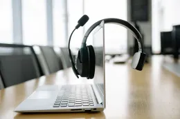 Professional communication headset mounted on a laptop display on a wooden conference table in a modern office.