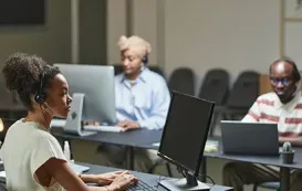 A call center agent wearing a headset, smiling while speaking to a customer in a modern office environment.