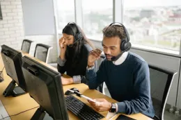 Customer service representatives with headsets working at computer desks in a modern open office space.