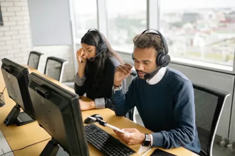 Customer service representatives with headsets working at computer desks in a modern open office space.