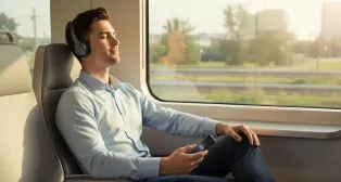 Man in business attire relaxes on a train journey, eyes closed, listening to a free music app without ads through a headset.
