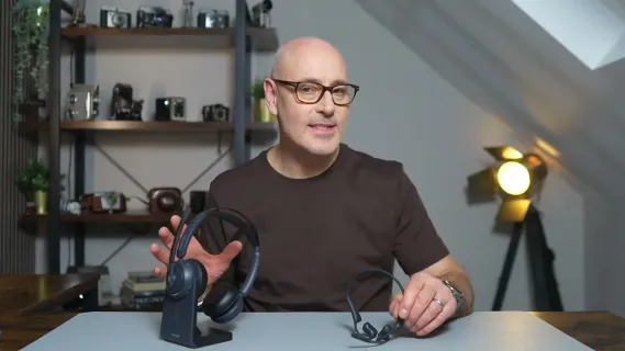Nuroum HP31D and OpenEar Pro 2 wireless headset with mic displayed on a desk as Tim sits behind them during a headset comparison review for work use