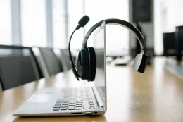 A black office headset with a microphone resting over the top of an open laptop screen in a modern office environment.