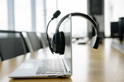 A black office headset with a microphone resting over the top of an open laptop screen in a modern office environment.