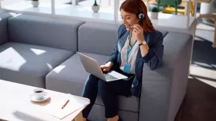 A professional woman wearing a noise-canceling call center headset while working in a busy real estate office, speaking with clients and managing property inquiries on her computer.