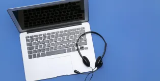 Black wired customer service headset with microphone resting on an open laptop keyboard against a blue background