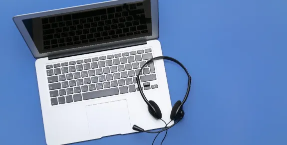 Black wired customer service headset with microphone resting on an open laptop keyboard against a blue background