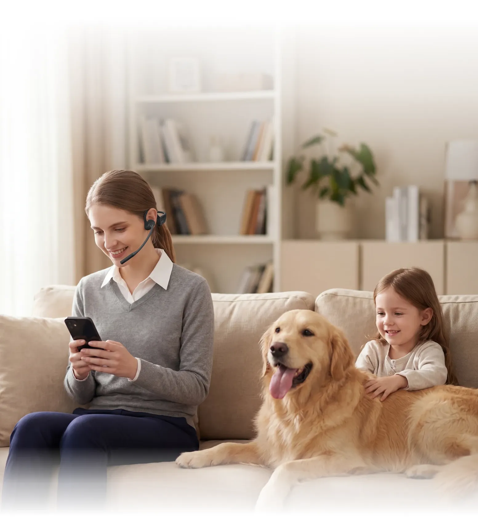 A smiling woman wearing a wireless open-ear headset looks at her smartphone on a living room sofa next to a young child and a golden retriever.