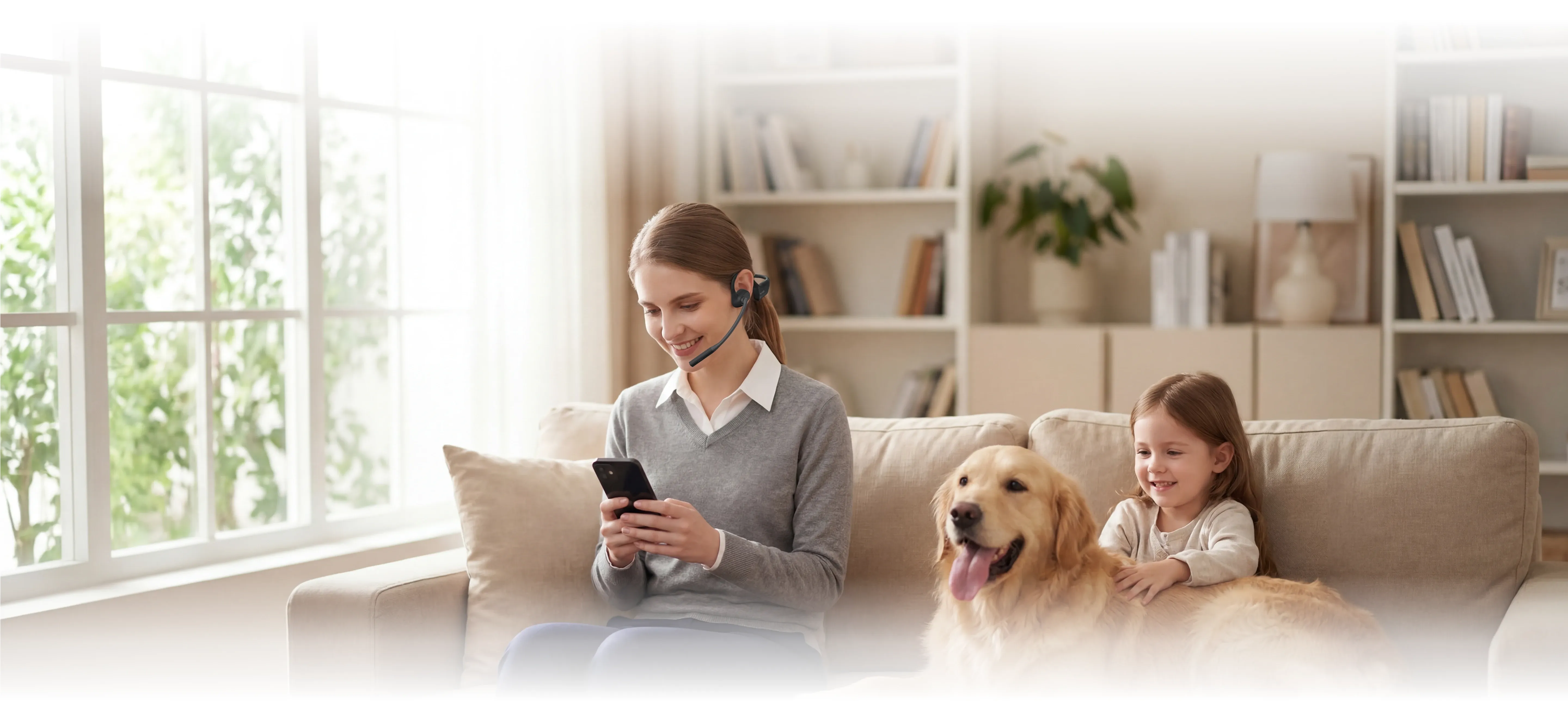 A smiling woman wearing a wireless open-ear headset looks at her smartphone on a living room sofa next to a young child and a golden retriever.